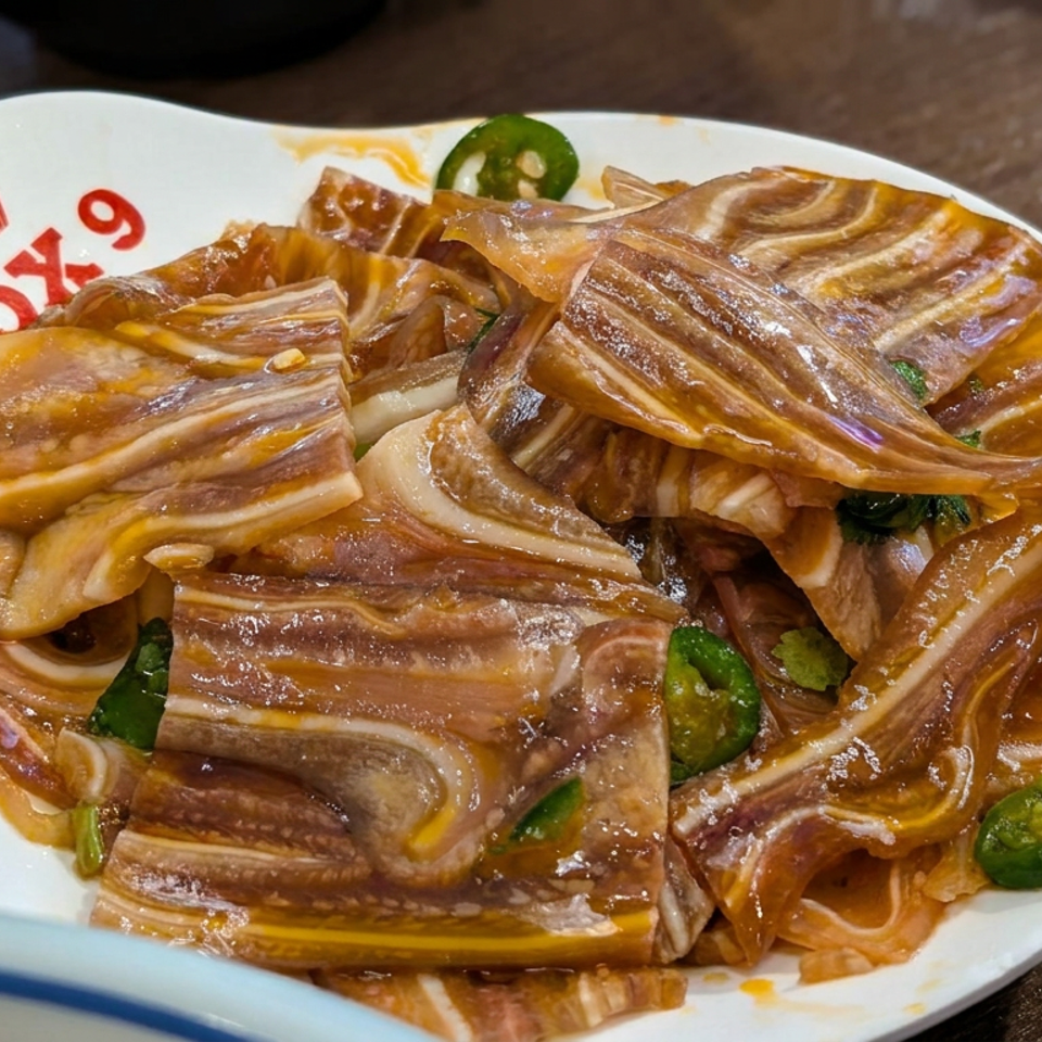 Plate of glossy braised, layered slices garnished with fresh green chili peppers on a wooden restaurant table.